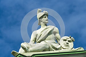 Ancient warrior sculpture sits and in the hands holds a circle disk with a face, a smiley.