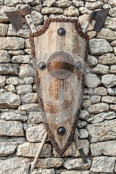 Ancient weapons on a stone wall. Wooden shield with iron accents