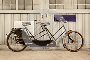 Ancient weathered tandem bicycle in front of an old factory door