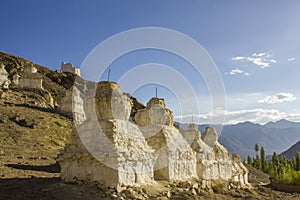 A ancient white holy Tibetan Buddhist temples on a desert mountain in the daytime against the backdrop of a mountain valley
