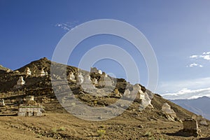 A ancient white Tibetan Buddhist temples stupas on the slope of a desert hill against the blue sky and mountain valley