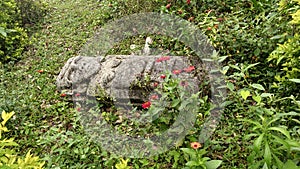 An ancient woman sculpture over grass with moss and red flowers at Colombian San Agustin archaeological park. photo