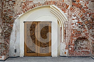 Ancient wooden church door with carvings of saints and red brick wall St. George the Martyr Church, Kaunas, Lithuania