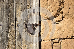 Ancient wooden door with a rusty padlock on a stone made wall