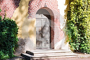 An ancient wooden door with steps with ivy of an abandoned tower or house.