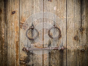 Ancient wooden gate with two door knocker rings and locks