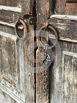 Ancient wooden gates with the round metal doorknobs and a hanging chain with a lock. Vertical orientation photo