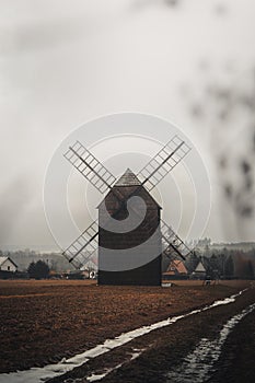 Ancient wooden mill standing alone in a field in gloomy foggy weather. Historical building for grinding corn, Opava, Czech