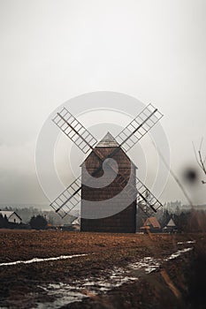 Ancient wooden mill standing alone in a field in gloomy foggy weather. Historical building for grinding corn, Opava, Czech