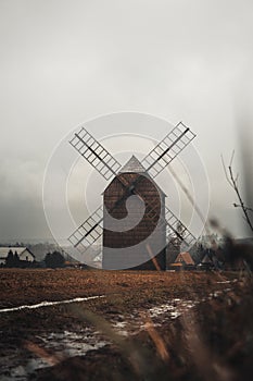 Ancient wooden mill standing alone in a field in gloomy foggy weather. Historical building for grinding corn, Opava, Czech