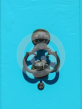 Ancient wrought iron door knocker on a blue background.