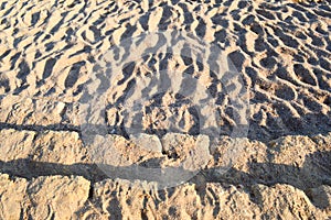 Ancient yellow stone steps covered with brown friable sand with waves and irregularities, descent to the beach. The background
