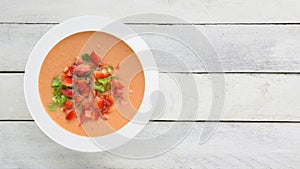 Andalusian gazpacho served in a white plate on a wooden table. Top view and empty copy space