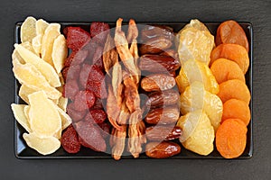 Ð¡andied slices of ginger root and strawberries, dried pear slices, dates, peaches and apricots lying on a black ceramic plate