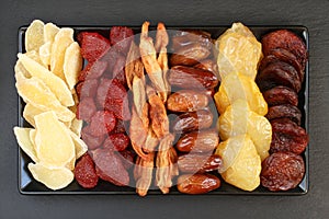 Ð¡andied slices of ginger root and strawberries, dried pear slices, dates, peaches and apricots lying on a black ceramic plate