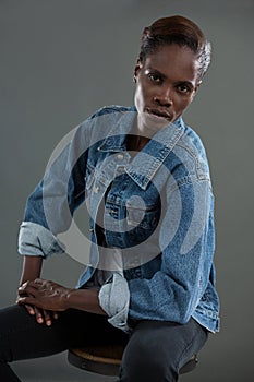 Androgynous man in denim jacket posing against grey background