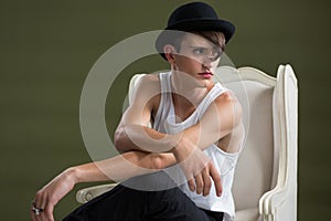 Androgynous man in hat sitting on chair