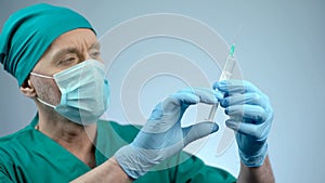 Anesthesiologist in face mask checking syringe for injection, operating theater