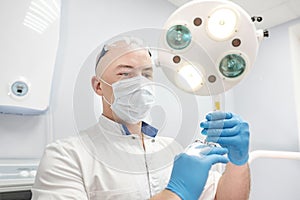 An anesthetist doctor holds a syringe in his hands and looks into the frame