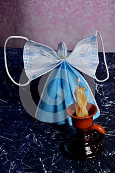 Angel from blue face protection mask burning candle and christmas decoration background