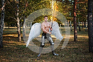 Angel, a bodybuilder in plate armor on his legs with wings behind his back, holds in his hands a fiery two-handed sword