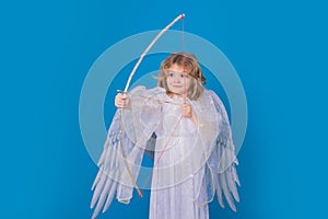 Angel with bow and arrow. Valentine& x27;s day. Blonde cute child with angel wings on a blue  studio background