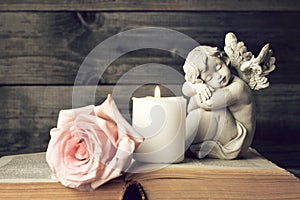 Angel, candle and pink rose on wooden background