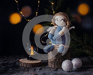 An angel crocheted sits on a stump with a lantern