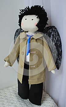 Angel doll with black wings, wear olive coat and blue tie.