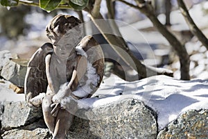 Angel figure sitting on a rock wall in the snow on a winter`s day