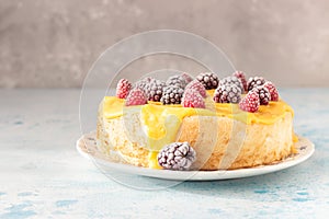 Angel food cake with lemon curd and frozen berries raspberry and blackberry on a plate, blue concrete background.