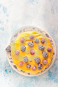 Angel food cake with lemon curd and frozen berries raspberry and blackberry on a plate, blue concrete background.