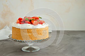 Angel food cake with whipped cream and slices of fresh strawberries on top on a concrete background. Summer dessert. Horizontal