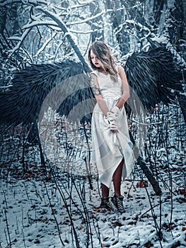 Angel girl with black wings in winter forest.