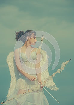 Angel girl in white angels dress with wings holding bow and arrow. Happy valentines day. Teen love and romance concept.