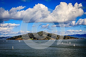 Angel Island with scattered sailboats and perfectly placed white clouds in a clear sunny day seen from Sausalito