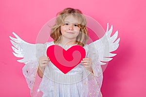 Angel kid with heart. Valentine's day. Blonde cute child with angel wings on a pink studio background. Happy angel