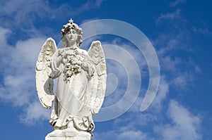 Angel statue standing against clouds blue sky at a Cemetery.