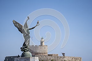 Angel Statue of Victory in Mandraki Harbour in in focus and in the background Saint Nicholas Fortress