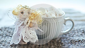 Angel in white lace dress with hands folded in prayer. homemade sock toy with fluffy red hair in background of window. cup of