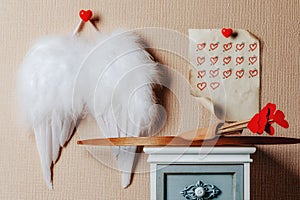 Angel wings hanging on the wall . Cupid weapons set bow and arrows on the nightstand.