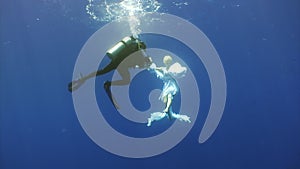 Angel young woman underwater model in white cloth and cameraman.