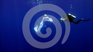 Angel young woman underwater model in white cloth and cameraman.