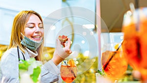 Angelic caucasian woman smiling and taking a bite during happy hour surrounded with colorful drinks. happy blonde girl wearing