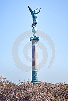 Angelic statue for the fallen in war saluting high on a column above blooming pink cherry flowers commemorates the death of war