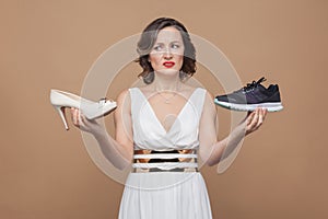 Anger woman in white dress holding high heels and sneakers and l