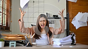 Angered, furious, crazy and mad Asian businesswoman throwing up papers at her desk