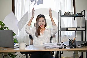 Angered, furious Asian businesswoman throwing up papers at her office desk