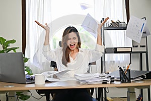 Angered and mad Asian businesswoman screaming and throwing up papers at her desk