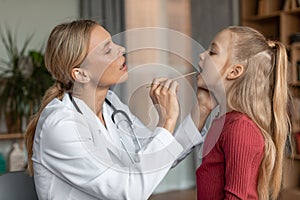 Angina, tonsillitis, cold and flu in children concept. Female doctor pediatrician checking patient little girl throat photo